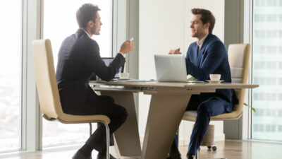 Dois homens de terno sentados em uma mesa conversando sobre as vantagens de contratar um ERP